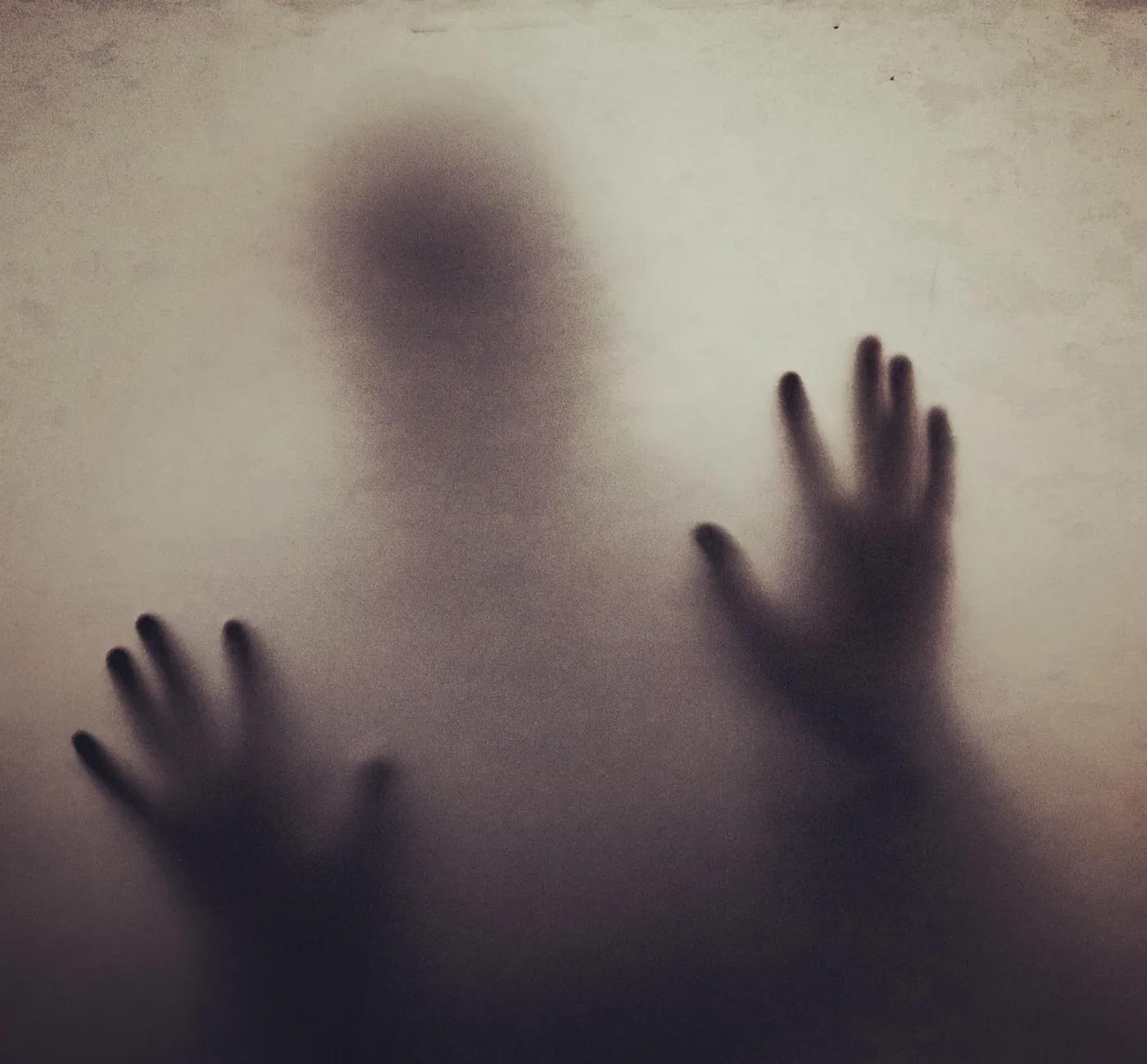 Silhouette of a person with hands pressed against frosted glass